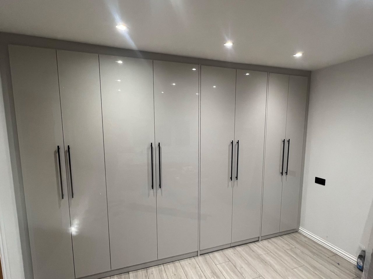 Full-height fitted wardrobes by the MALCON team in a light grey gloss finish with black bar handles