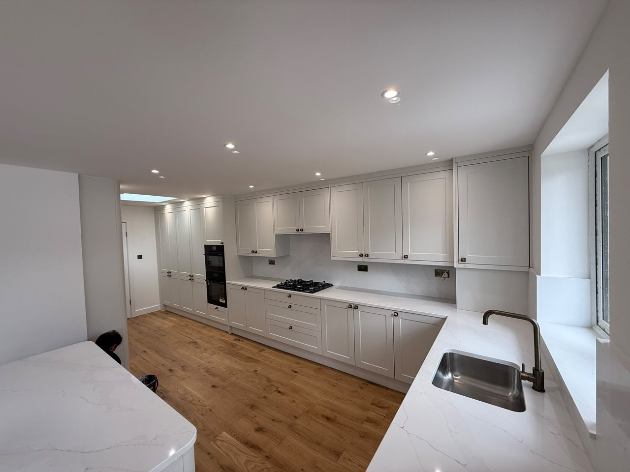 White Shaker-style kitchen by the MALCON team with stone-effect worktops, integrated ovens and an oak floor